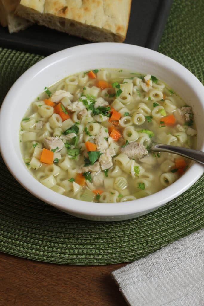 A white bowl of PRessure Cooker Chicken Noodle Soup sits on a green surface.