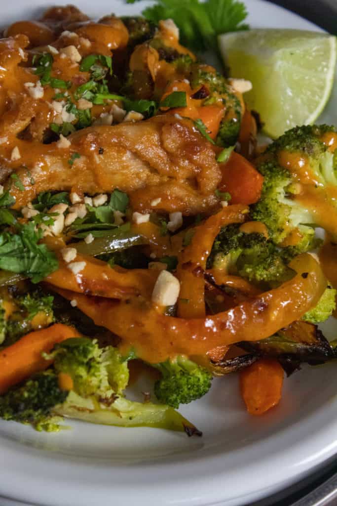 A close shot of chciken and vegetables with crushed peanuts and peanut sauce.