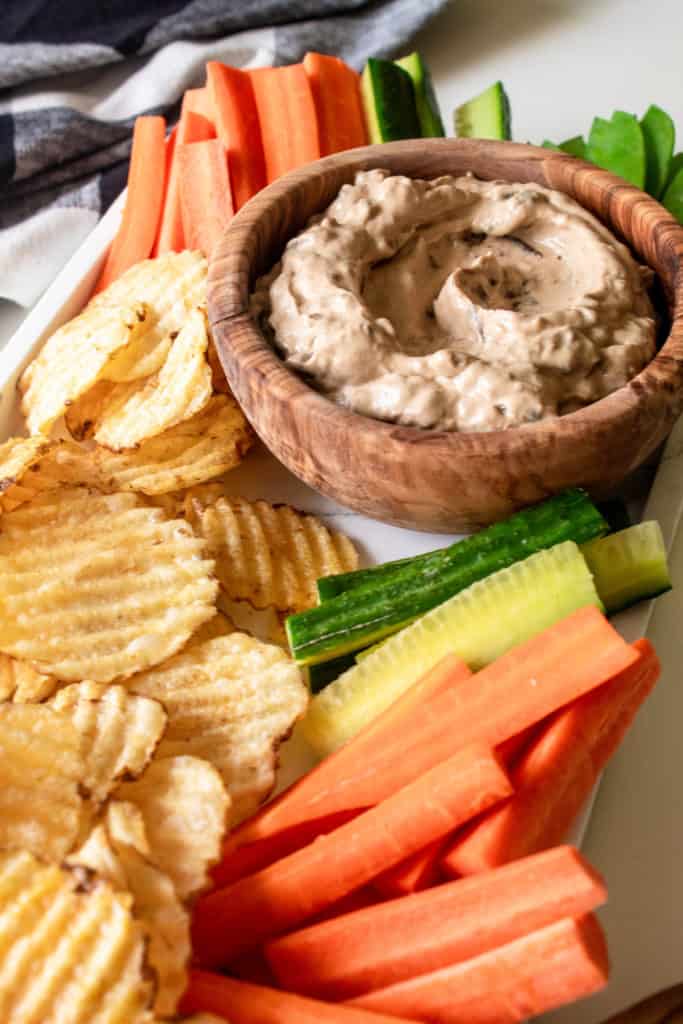 Caramelized Onion Dip in a wooden bowl surrounded by chips and vegetables on a white tray.