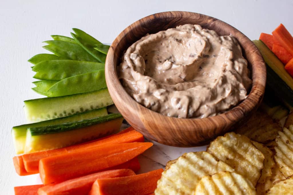 A tray of Caramelized Onion Dip surrounded by vegetables and potato chips.