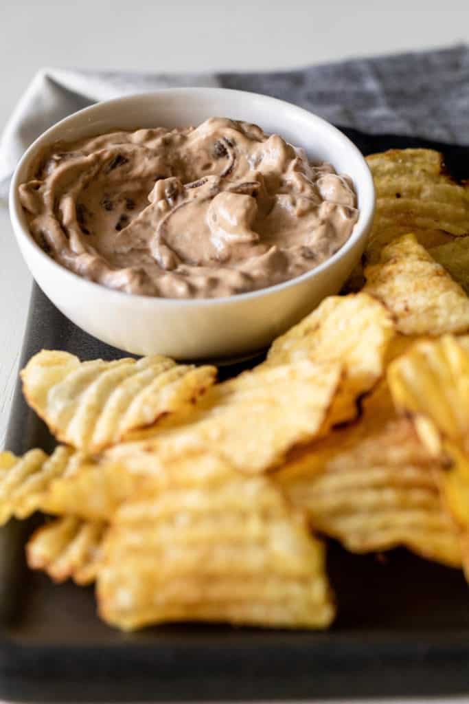 A white bowl of Caramelized Onion Dip surrounded by potato chips.
