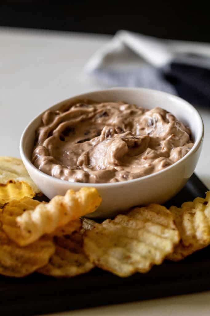 A white bowl of Caramelized Onion Dip surrounded by potato chips.