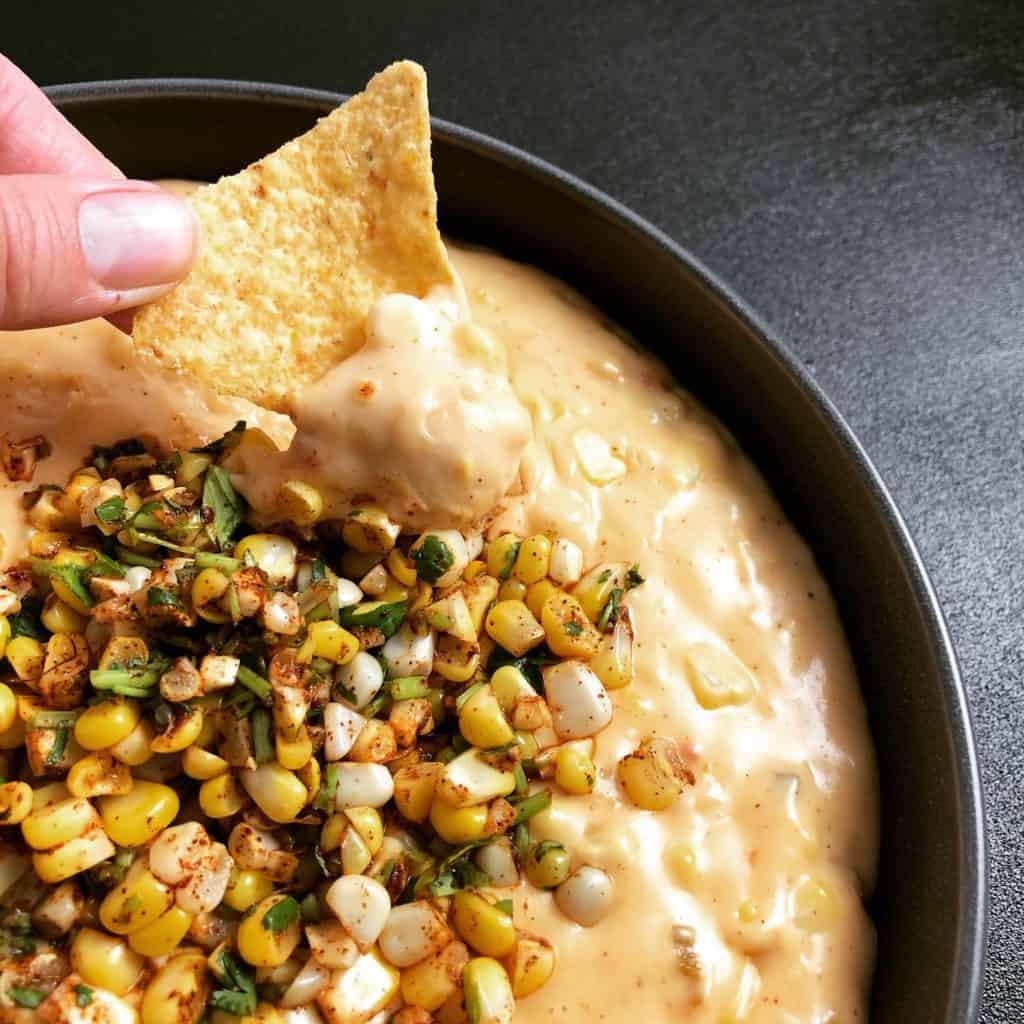 A close-up shot of a bowl of queso topped with spiced corn kernels.