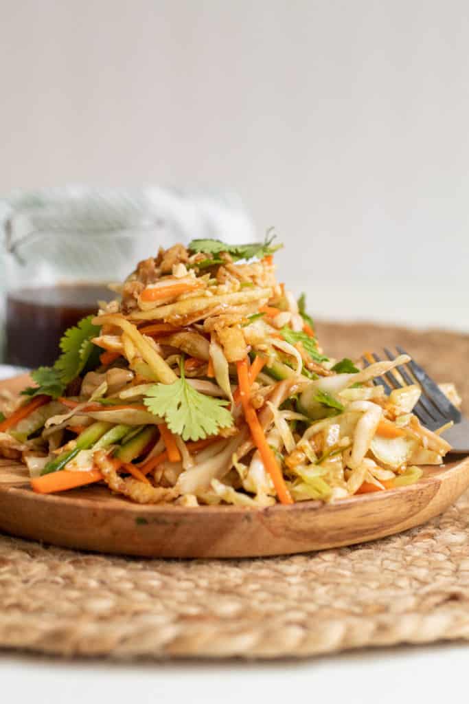 The Chicken and Cabbage Salad with Hoisin Vinaigrette is piled on a wood plate on a woven place mat.