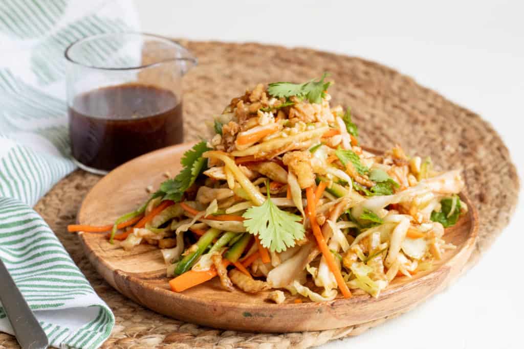 Chicken and Cabbage Salad with Hoisin Vinaigrette on a brown wooden plate with a white background.