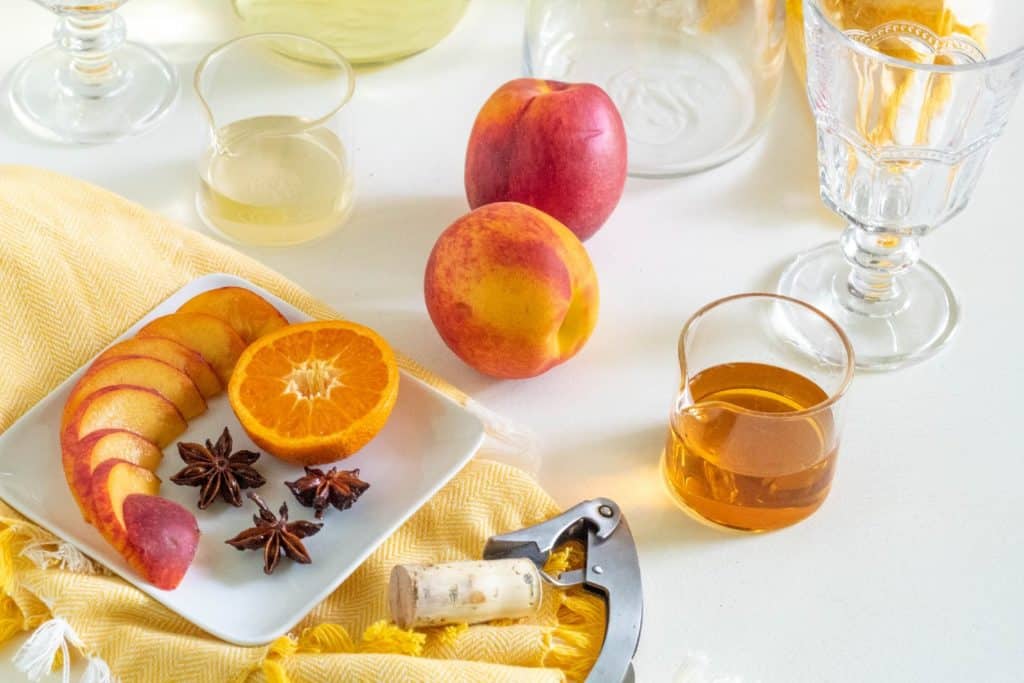 A plate of fruit and star anise garnish alongside a cork and bottle opener and a beaker of brandy.