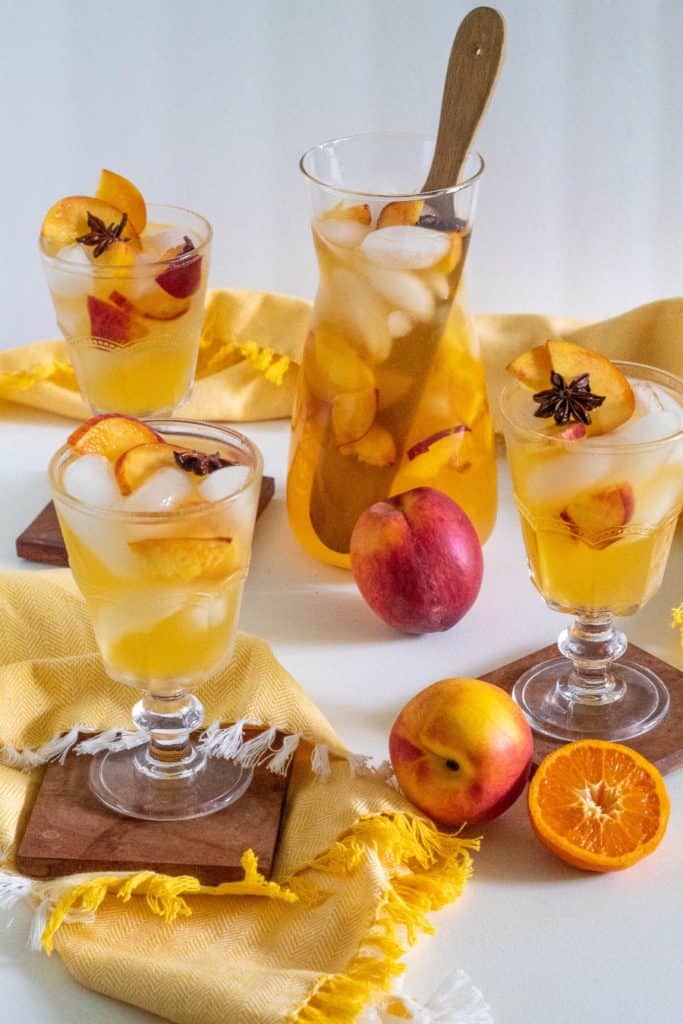 A pitcher of stone fruit sangria and three glasses with fruit in the foreground.