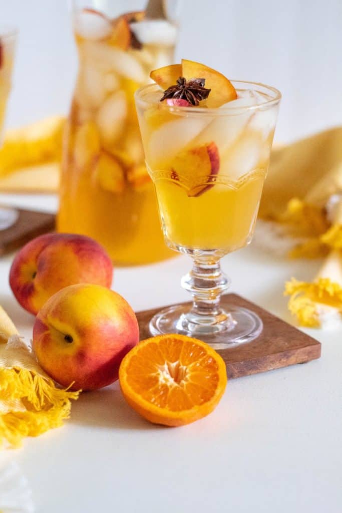 A glass of stone fruit sangria with fruit in the foreground.