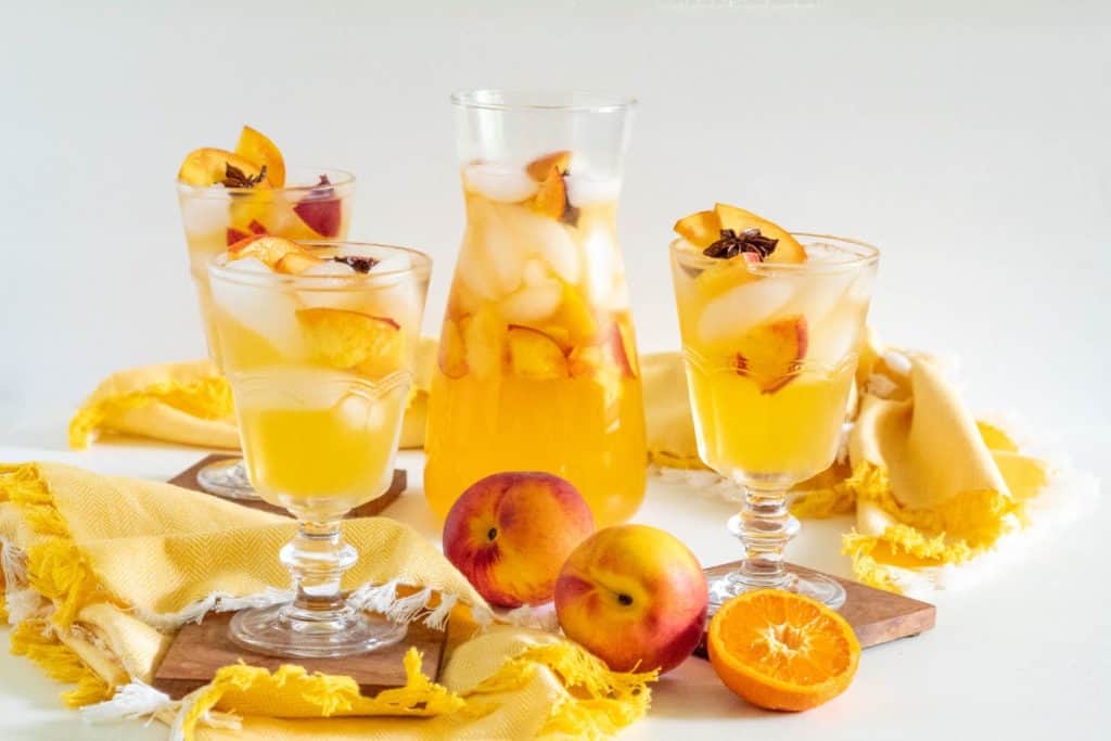 A pitcher of stone fruit sangria and three glasses with fruit in the foreground.