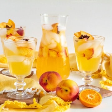 A pitcher of stone fruit sangria and three glasses with fruit in the foreground.