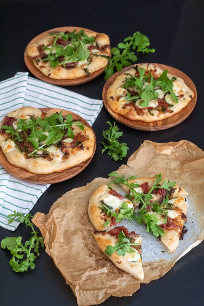 Cooked pizzas garnished with arugula are arranged on a black surface with a green and white striped napkin.