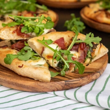 A detail photo of a slice of Caramelized Onion and Prosciutto Pizza on a wooden plate.