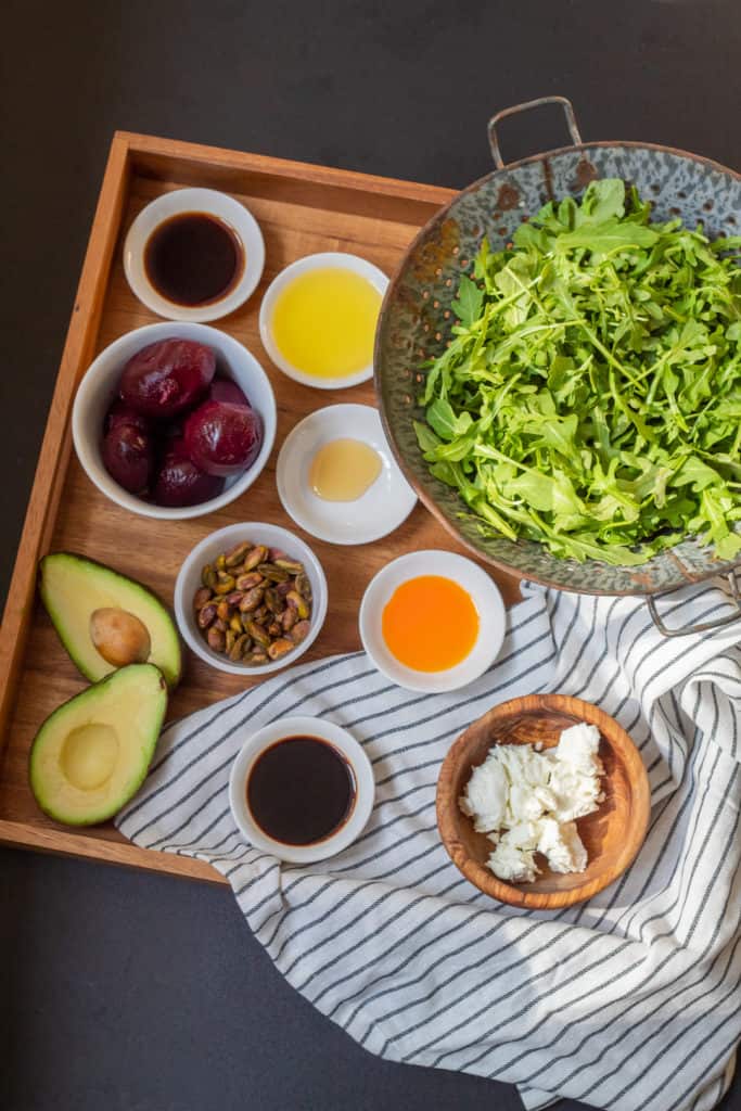 Ingredients for Beet and Avocado Salad with Chili-Soy Vinaigrette are arranged on a square wood platter with a black and white napkin. The platter sits on a black surface.