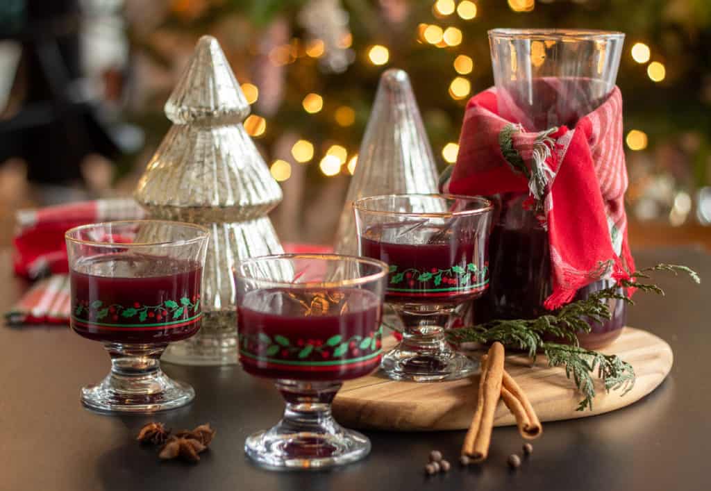Three glasses of a red beverage sit on a black surface with a holiday backdrop..