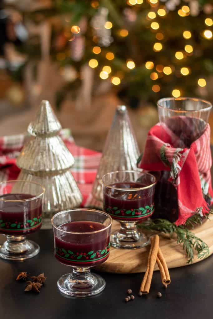 A carafe of Mulled Wine sits on a wooden board with three glasses of mulled wine nearby.
