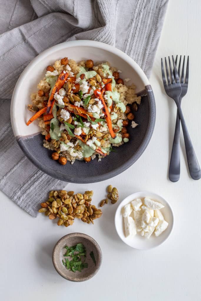 Extra toppings for the grain bowls sit alongside a serving on a white surface.