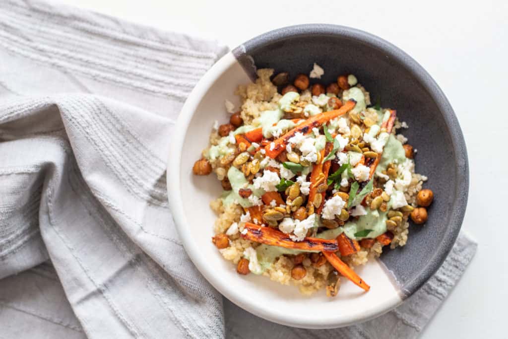 A shallow bowl of grains and carrots sits on a gray towel.