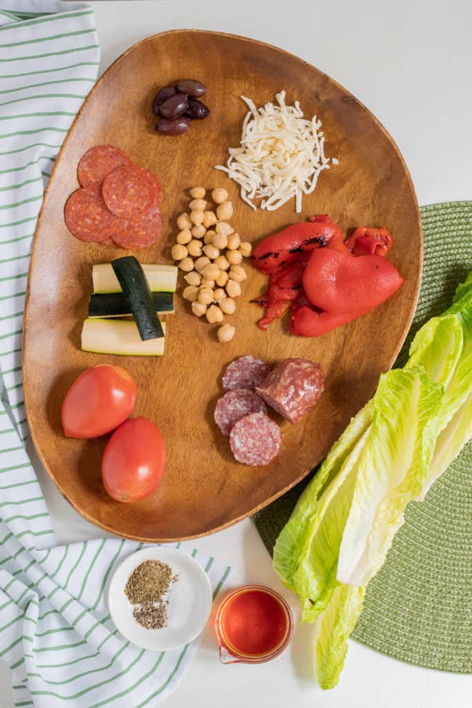Ingredients for Antipasto Chopped Salad are arranged on a wooden platter.