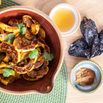 A bowl of golden squash is on teh left of the image. Small bowls of honey and spices are to the right of the bowl, next to two dried chiles.