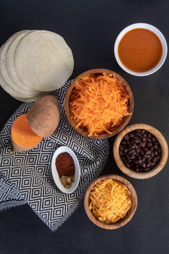 Ingredients for Black Bean and Sweet Potato Stacked Enchiladas are arranged on a black surface.