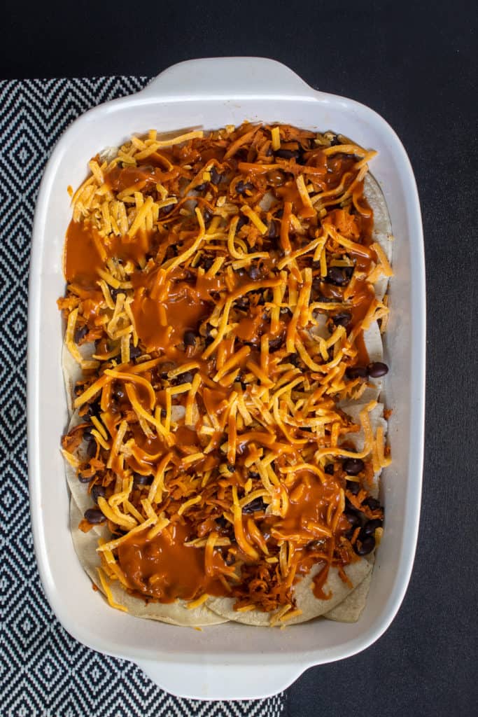 One layer of stacked enchiladas is demonstrated in a white baking dish on a black surface.