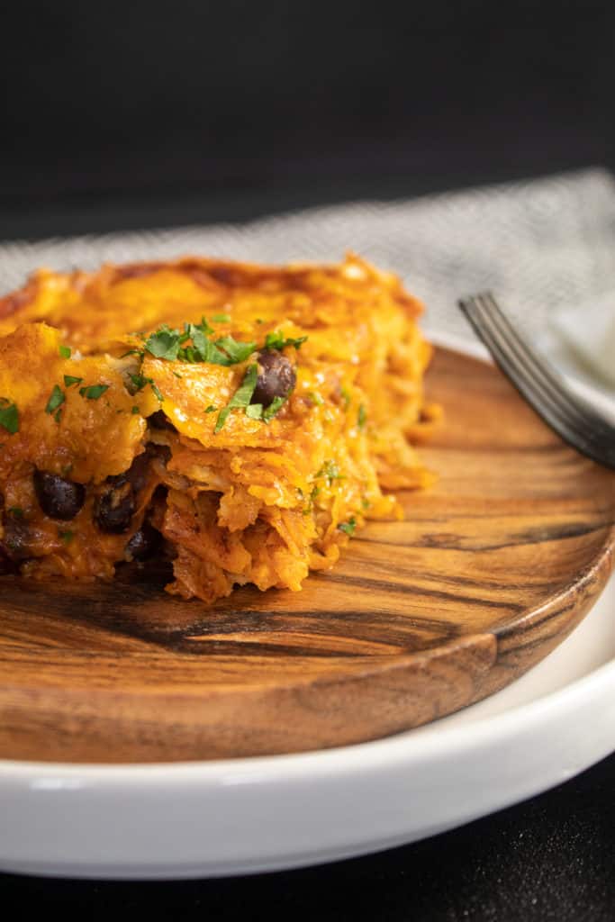 An up close photo of a serving of enchilada on a wooden plate shows the layers and texture.