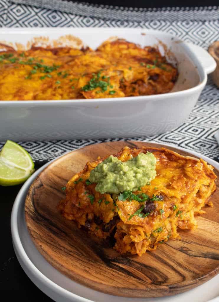 A serving of Black Bean and Sweet Potato Stacked Enchiladas is in the foreground with the baking dish in the background.