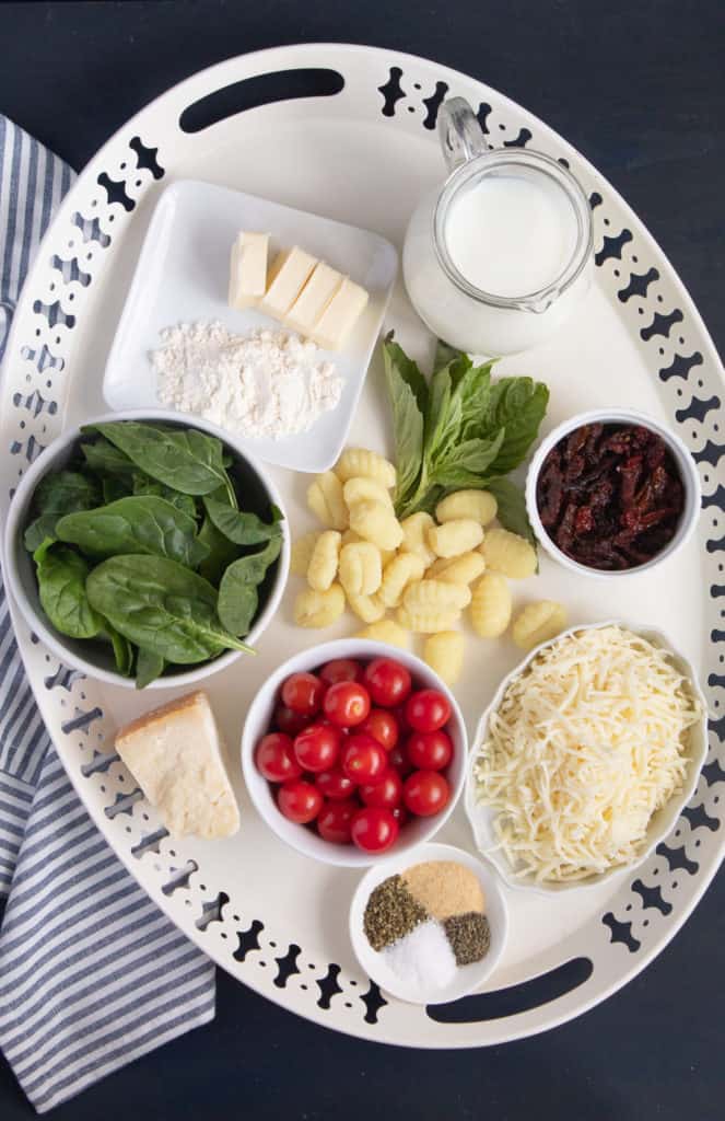 Ingredients for Baked Gnocchi with Sun Dried Tomato Cream are arranged on a white serving platter over a blue background.