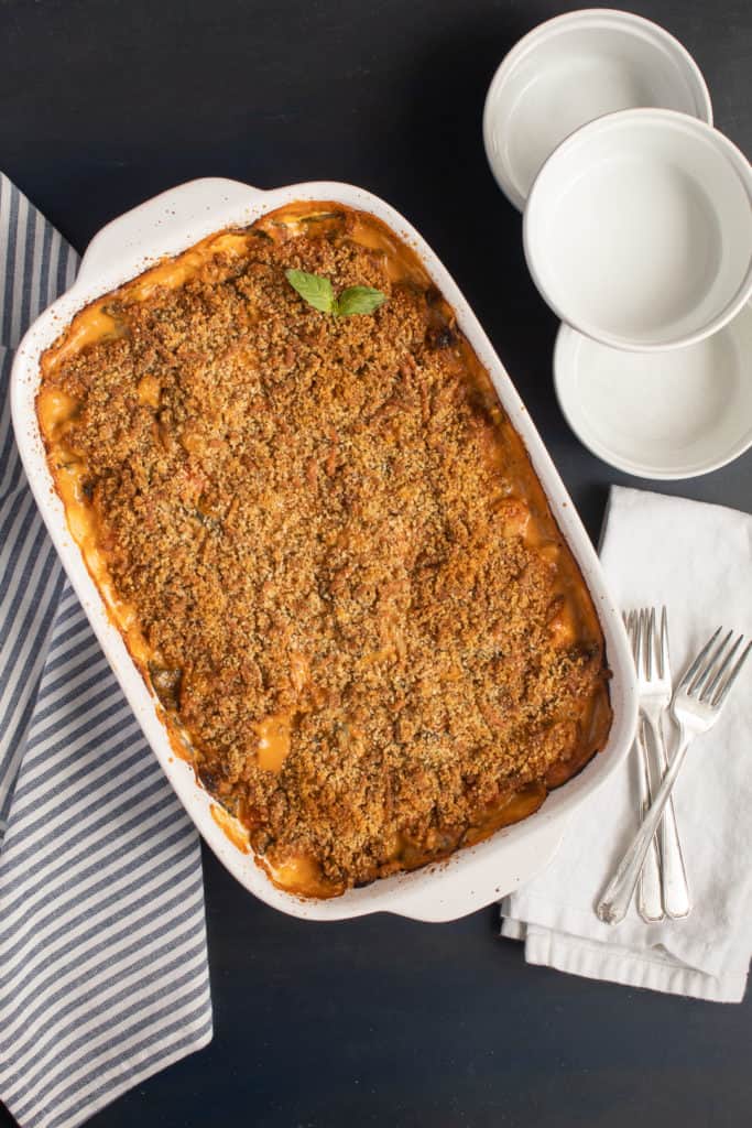 A baking dish of the Baked Gnocchi with Sun Dried Tomato Cream sits on a blue background with serving bowls and utensils alongside.