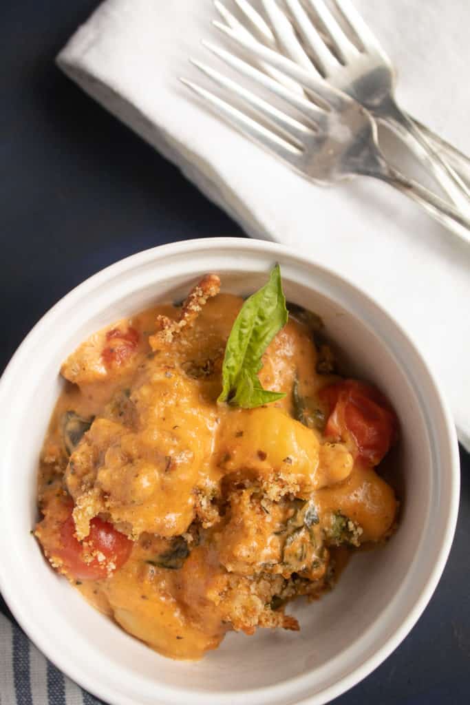 A serving of gnocchi in a red-orange sauce is in a small white bowl over a blue background.