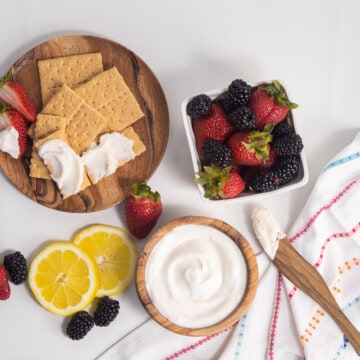 Graham crackers, lemons, and berries are arranged on a white background along with a bowl of white sauce.