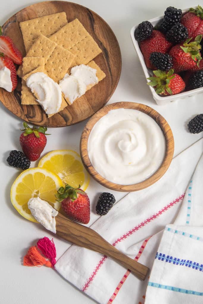 Graham crackers, lemons, and berries are arranged on a white background along with a bowl of white sauce.