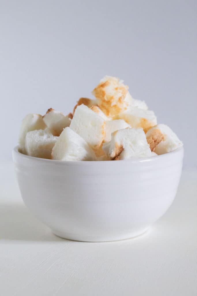 Cubed angel food cake in a white bowl on a white surface.