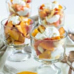 Individual cups of sliced peached, whipped cream, and angel food croutons arranged on a white surface.