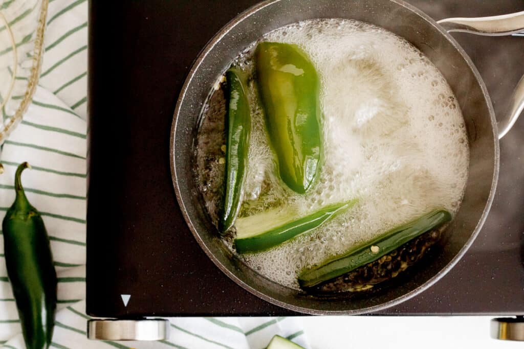 Halved jalapenos boiling in simple syrup on a black cooktop.
