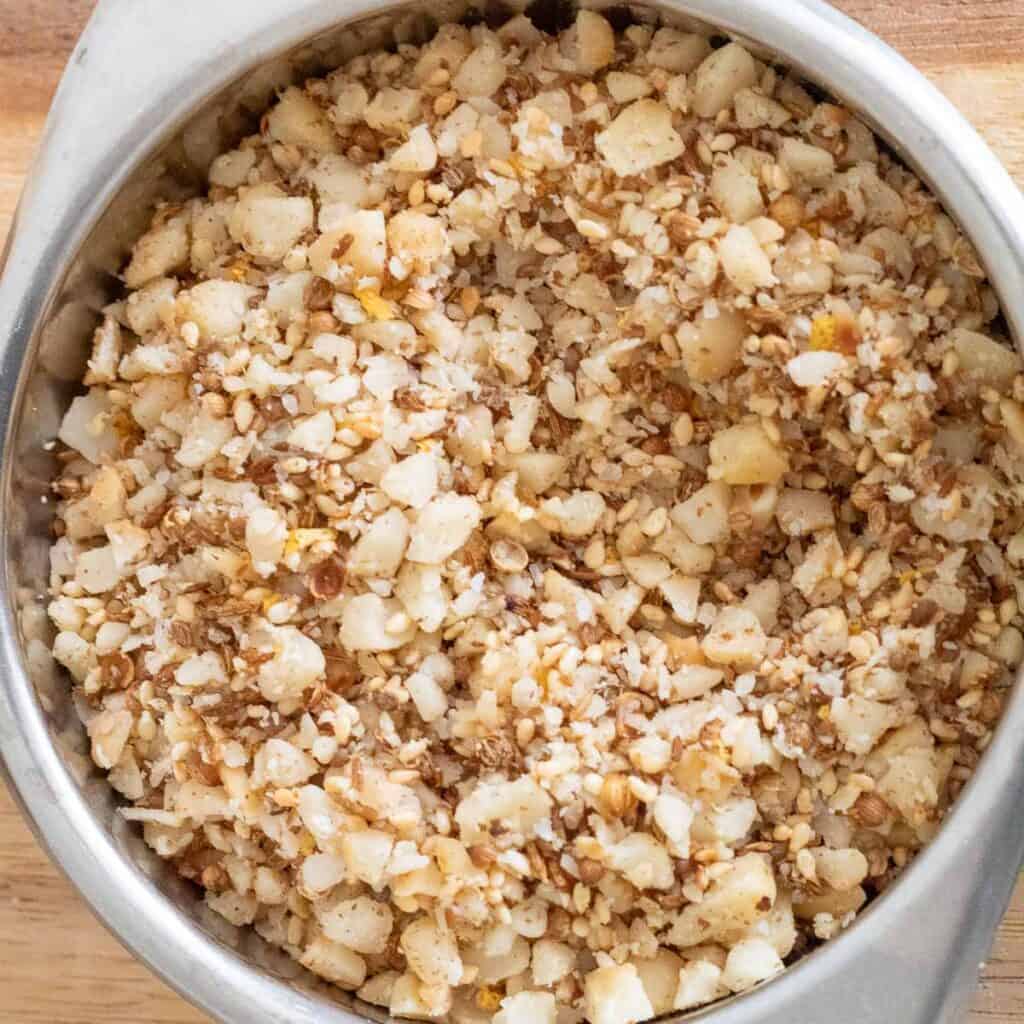 A brown mixture of seeds, nuts, and coarsely ground spices in a silver bowl.