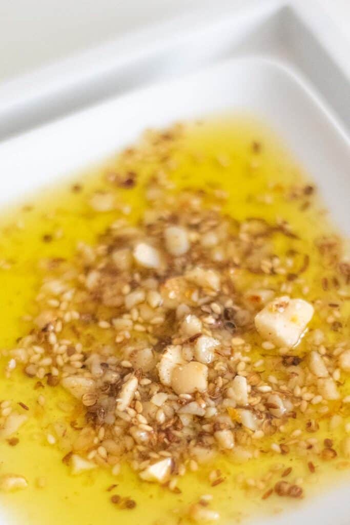 Macadamia dukkah sits in a pool of olive oil on a white dish.