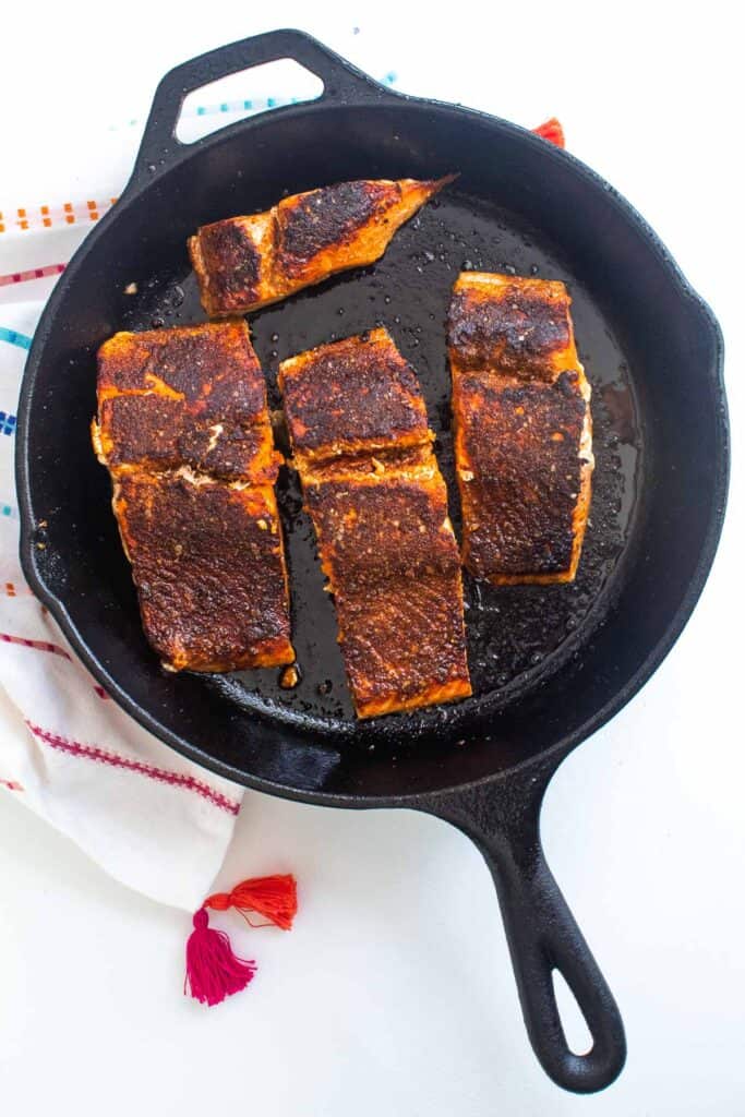 seared salmon filets in a cast iron skillet on a white surface.