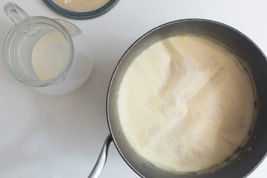 The steeped cream mixture cooling in a gray sauce pan with a circle of parchment covering the top.