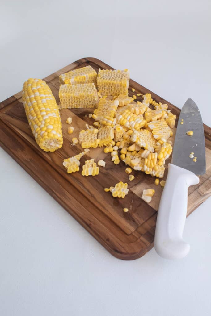 Corn cut off of the cob on a wooden cutting board.
