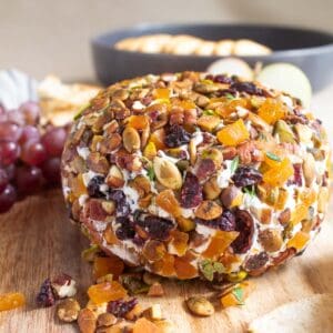 The finished cranberry and goat cheese ball wrapped in chopped apricots, cranberries, pecans, pistachios, pepitas, and thyme presented on a wood platter.
