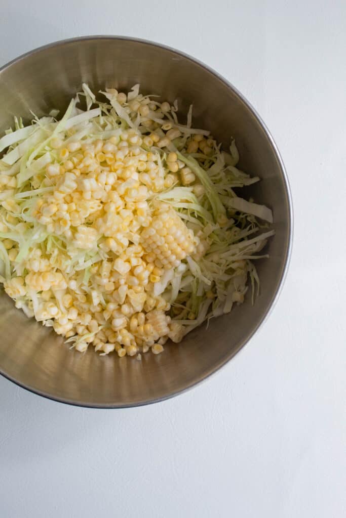 Finely shredded cabbage and corn kernels in a silver bowl.