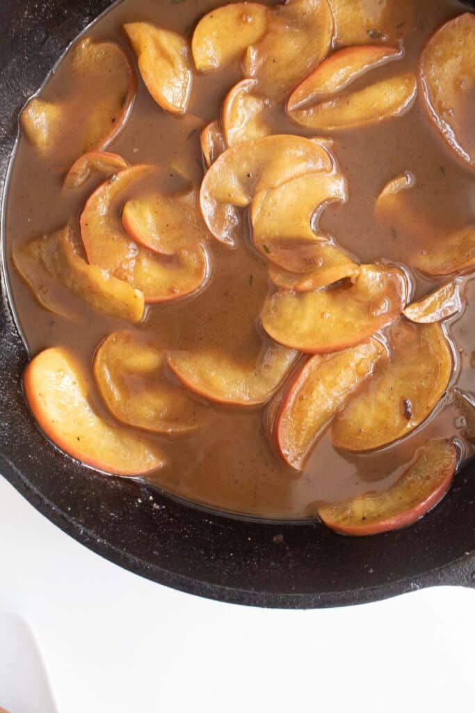 Silky brown sauce surrounding sliced apples in a cast iron skillet.