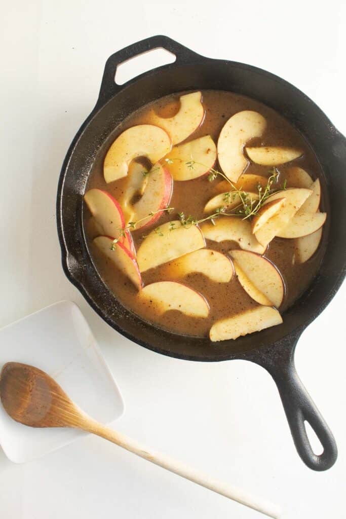 Apples, thyme, and cider are combined in a cast iron skillet to make the apple cider gravy.
