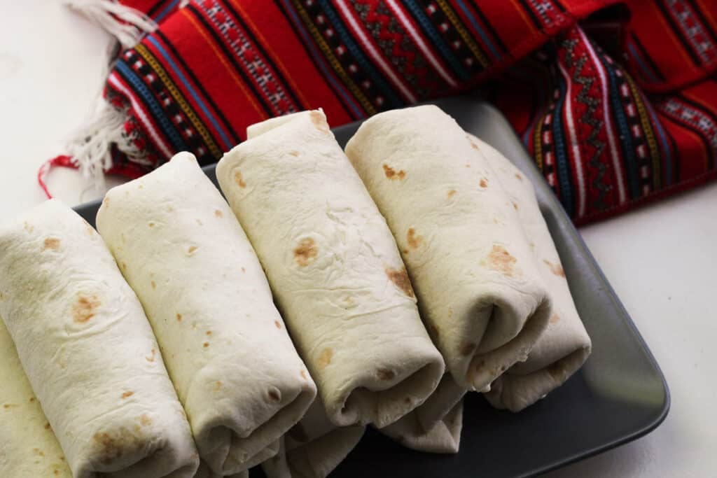 A pile of wrapped burritos on a gray platter.