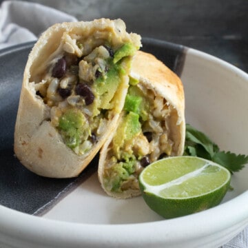A black and white bowl with a burrito with green avocado and black beans in the filling.