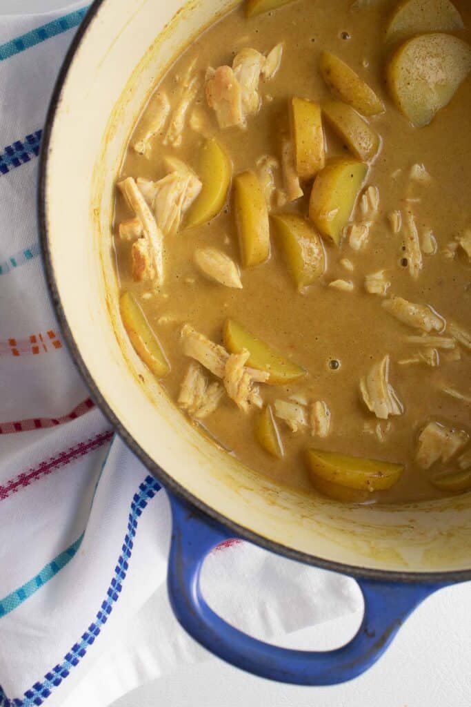 A yellow mixture containing potatoes and shredded turkey sits in a blue pot.