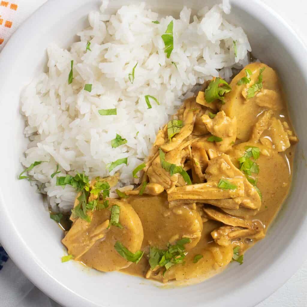 A white bowl containing rice, a golden sauce with potatoes and meat, and green chopped herbs.