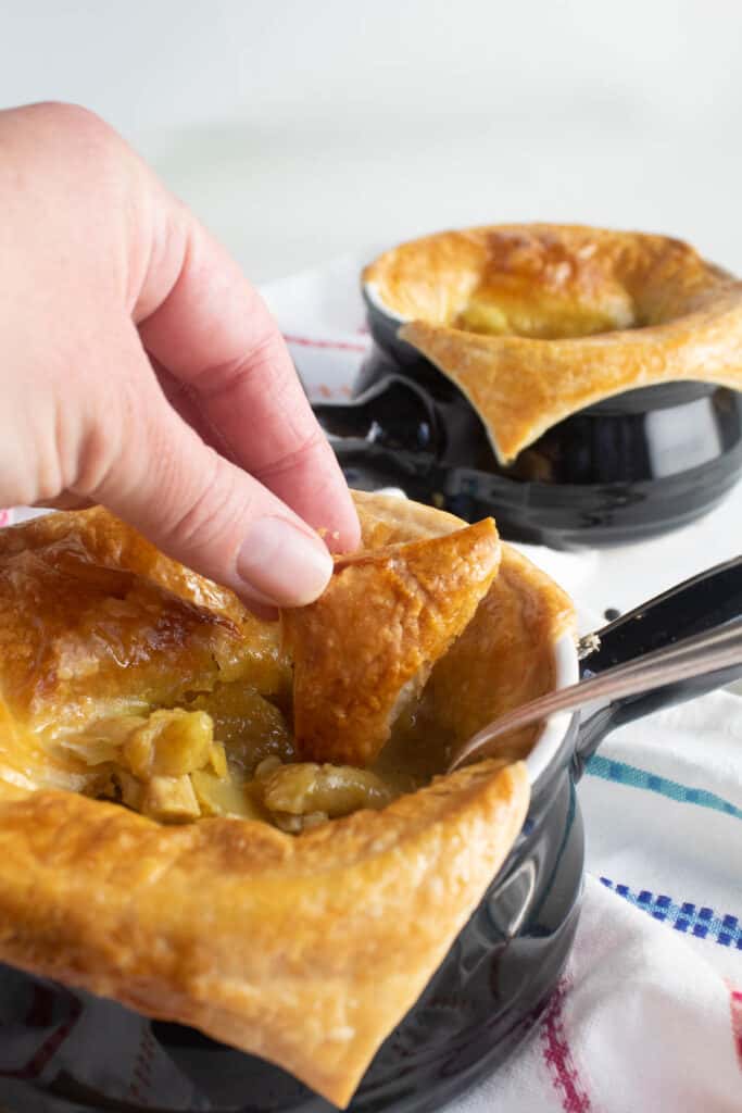A hand dipping baked puff pastry into a bowl of golden sauce.