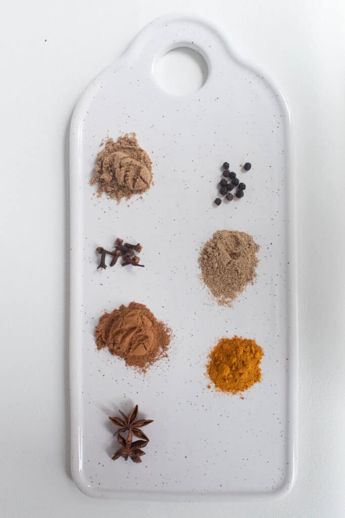 Ground and whole spices mounded on a white serving tray.